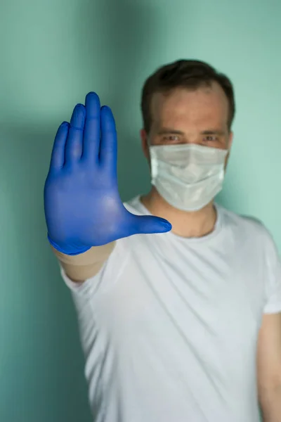 Porträtt av attraktiv man i medicinsk mask och en handske på blå bakgrund. Begreppet pandemiskt skydd. Stoppa koronovirus. Övergångsbestämmelser — Stockfoto