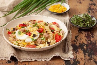 Sebzeli makarna salatası, yumurta ve ton balığı ahşap masada.