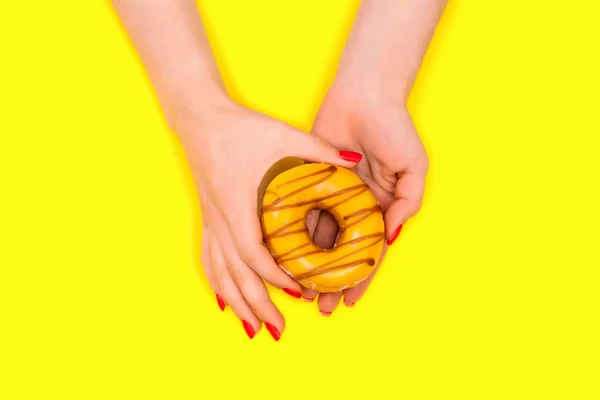 Hands of a beautiful woman holds a sweet yellow donut. Flat lay. — Stock Photo, Image
