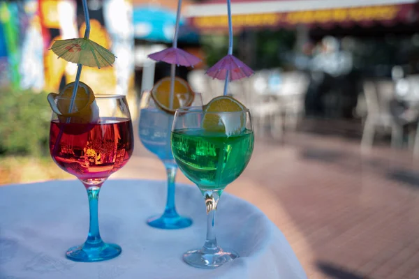 colorful cocktails with umbrellas and pieces of fruit are on the street on the table in a cafe in summertime  daylight