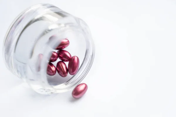 Cuidado conceito natural, frasco feito de vidro com pílulas vermelhas no fundo branco — Fotografia de Stock