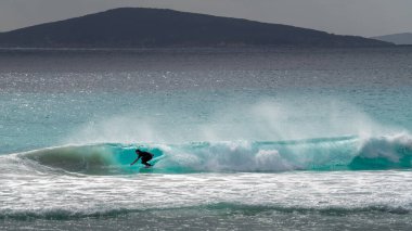 Cape Le Grand Beach, Batı Avustralya - 15 Ocak 2020: Erkek sörfçü yeşil dalgada kıyı esintisi ile su püskürterek arka planda tepeler oluşturan çömelmiş şekilde çömeliyor