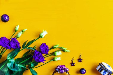 Purple flowers and womens accessories and jewelry on a yellow wooden background