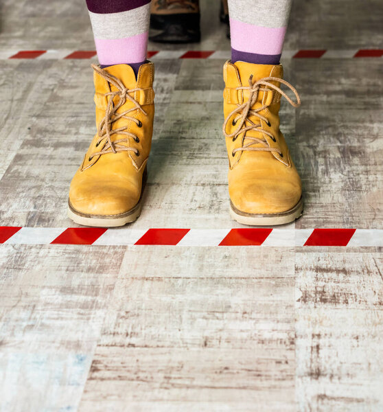 Ноги в жёлтых сапогах на магнитной ленте. Социальная дистанция во время эпидемии коронавируса
