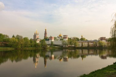 Moskova 'daki Novodevichy Manastırı, Rusya' nın bulutlu günbatımında. Sudaki yansımalar
