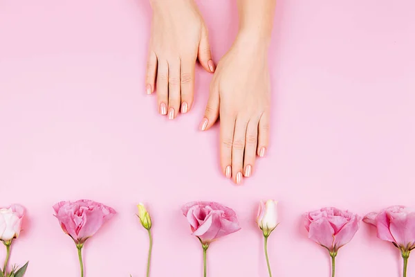 Mãos de mulher bonita com eustoma fresco. Conceito de Spa e Manicure. Mãos femininas com manicure rosa. Conceito de cuidados com a pele macia. Unhas bonitas. Sobre fundo bege — Fotografia de Stock