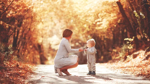 Young mother plays with her son in the autumn forest. Blond in a sports gray suit. Autumn leaves. Joyful family in nature. — Stock Photo, Image