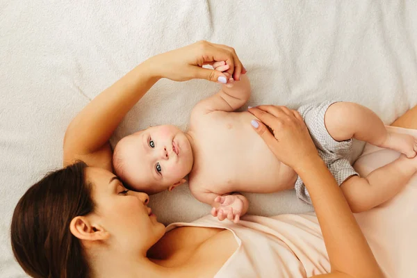 Giovane bella madre si trova con il bambino sul letto, bacia delicatamente, dormire insieme — Foto Stock
