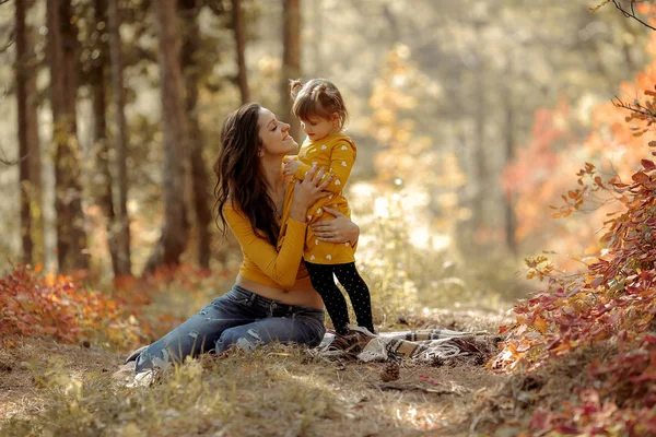 Die schöne junge Mutter und ihre glückliche Tochter amüsieren sich bei Sonnenuntergang im Wald. sie halten sich an den Händen und lachen — Stockfoto