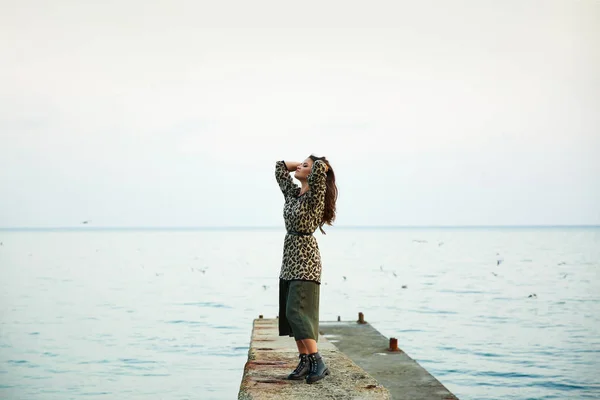 Joven mujer hermosa cerca del mar. disfruta de la naturaleza y la libertad. levantó las manos y coge la brisa del mar. tiene una falda larga y suéter con un adorno de leopardo de moda . — Foto de Stock
