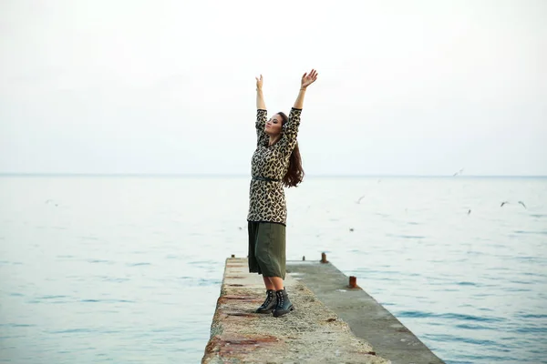 Joven mujer hermosa cerca del mar. disfruta de la naturaleza y la libertad. levantó las manos y coge la brisa del mar. tiene una falda larga y suéter con un adorno de leopardo de moda . — Foto de Stock