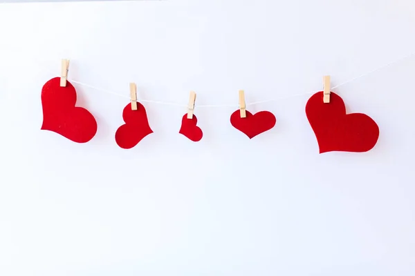 Rote Herzen auf Wäscheklammern auf weißem Hintergrund. Konzept des Valentinstages, Wäscheklammern und rote Holzherzen am Seil. — Stockfoto