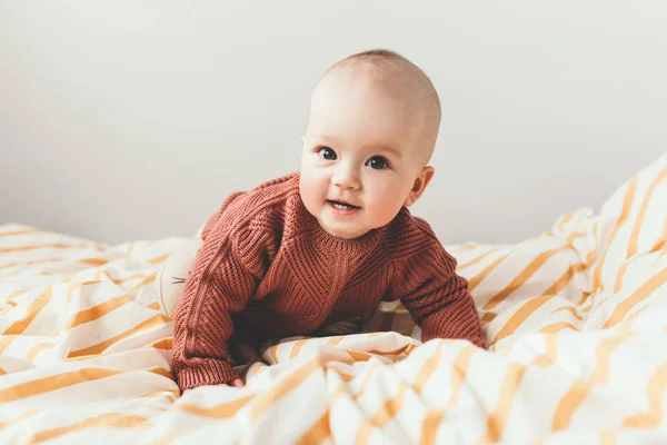 Linda menina na cama em um acolhedor sorriso camisola marrom. Conceito de maternidade e infância — Fotografia de Stock