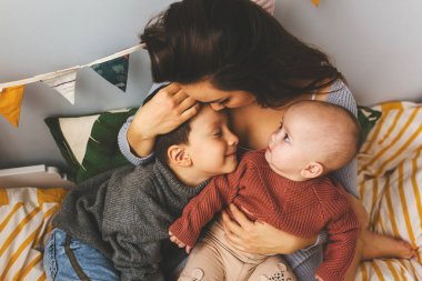 Genç, güzel bir anne, çocukları yataktayken, oğluna ve küçük kızına sıkıca sarılıyor, alnından öpüyor, çocuklar gülüyor..