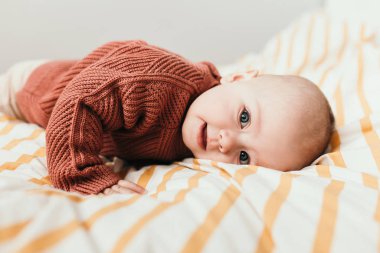 Yatakta, kahverengi süveteriyle gülümseyen güzel küçük bir kız bebek. Annelik ve çocukluk kavramı