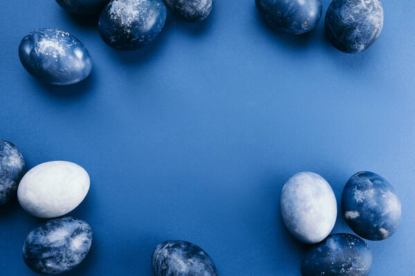 Beautiful group ombre blue Easter eggs with quail eggs and feathers on a blue background. Easter concept. Border eggs. Copy space for text.