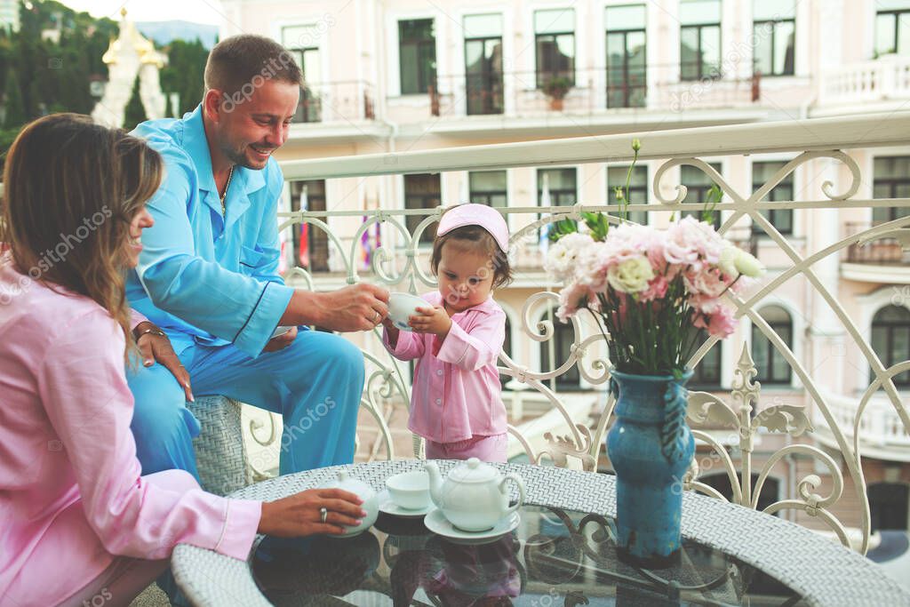 beautiful family on the balcony of the hotel enjoys the city view, in the nightgowns breakfast at the hotel, happy young parents with a child.