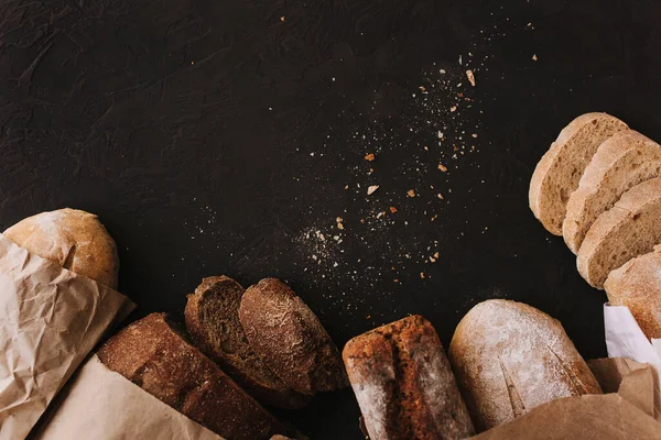 Vários pães crocantes e pães na mesa de pedra, Pão de pão de centeio fatiado artesanal cozido no forno fresco sobre fundo de textura escura. Vista superior, espaço de cópia — Fotografia de Stock