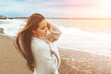 Sahilde temiz hava soluyan bir kadının yan görüntüsü. Yaz akşamları okyanusun kenarında otururken rahatlatıcı genç bir kadının yarım boy portresi, kaygısız çekici bir kadın.