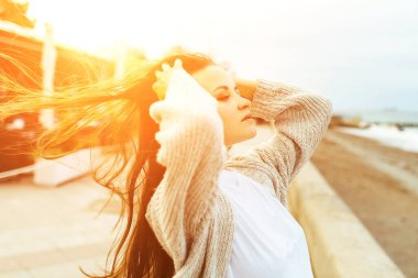 Sahilde temiz hava soluyan bir kadının yan görüntüsü. Yaz akşamları okyanusun kenarında otururken rahatlatıcı genç bir kadının yarım boy portresi, kaygısız çekici bir kadın.