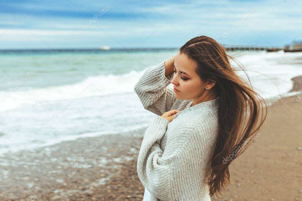 Side view portrait of a woman relaxing breathing fresh air on the beach. Half length portrait of young charming woman in relaxing while sitting near ocean in summer evening, attractive carefree female