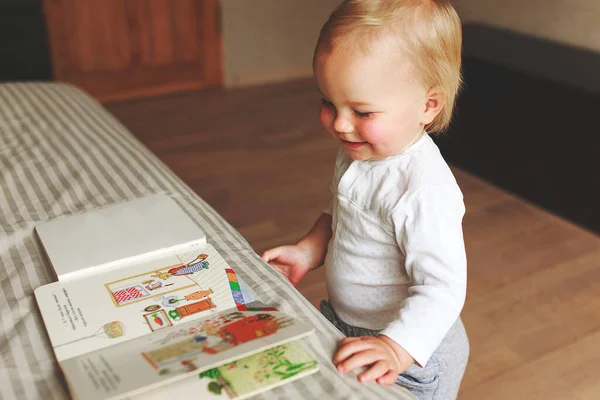 Baby boy turns the page in the book at home. He is very happy and excited by watching pictures. Child concept. quarantine time