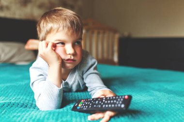 Evde pijamalı sıkıcı bir çocuk uzanıp televizyon izliyor..