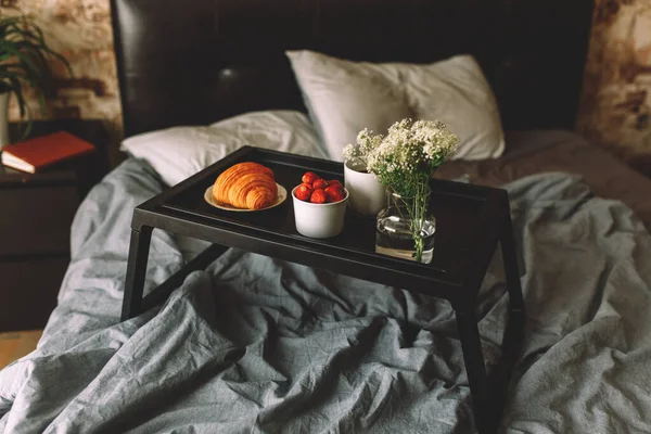 Breakfast on a tray in bed at home white dark linen. croissant tea strawberries — Stock Photo, Image