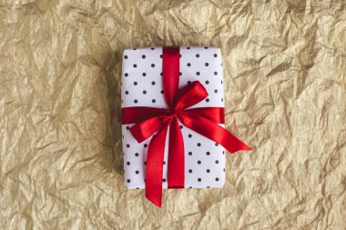 Altın folyo kaplamalı kırmızı fiyonklu siyah benekli beyaz kağıda sarılı bir hediye kutusu. Tatil kavramı. 