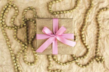 Altın arkaplanda pembe kurdeleyle süslenmiş altın hediye kutusu. Tatil kavramı. 