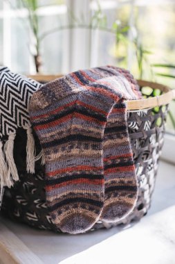 Güneşli bir günde pencerenin yanındaki sepette bir çift el örgüsü renkli çorap..