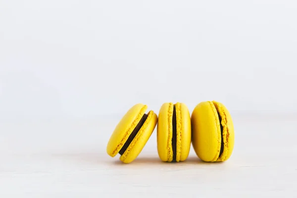 Trois macarons jaunes sur une table en bois. Macarons banane à la crème au chocolat. Fond blanc . — Photo