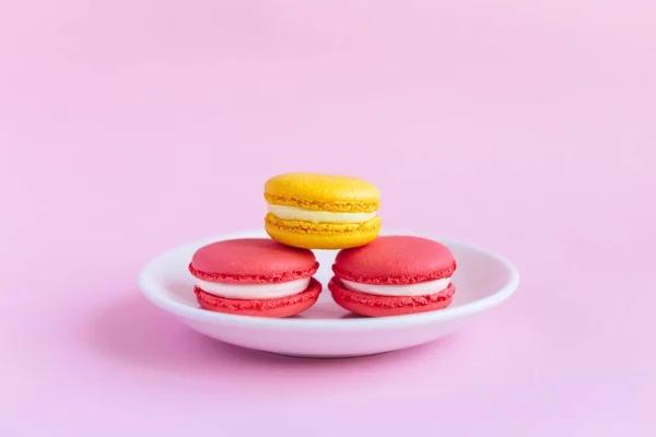 Tres sabrosos macarrones franceses en un plato blanco. Macarrones rosados y amarillos. Fondo rosa . — Foto de Stock