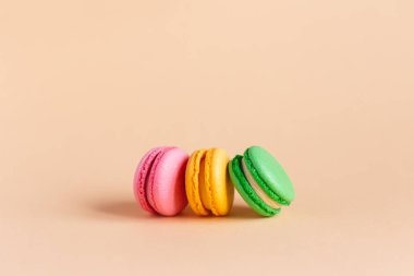 Şeftalili pastel arka planda üç lezzetli Fransız badem kurabiyesi. Pembe, sarı ve yeşil makaronlar..