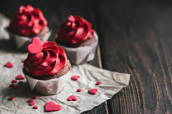 Magdalenas de San Valentín en color rojo, decoradas con corazones dulces en mesa de madera oscura . — Foto de Stock