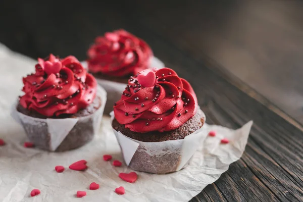 Magdalenas de San Valentín en color rojo, decoradas con corazones dulces en mesa de madera oscura . — Foto de Stock