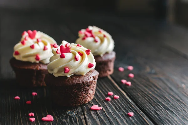 Magdalenas de San Valentín, decoradas con corazones dulces sobre una mesa de madera oscura . — Foto de Stock