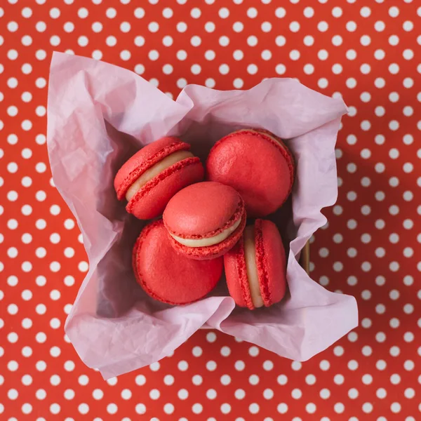 Macarrones franceses rojos en una caja sobre un fondo rojo con lunares blancos  . — Foto de Stock