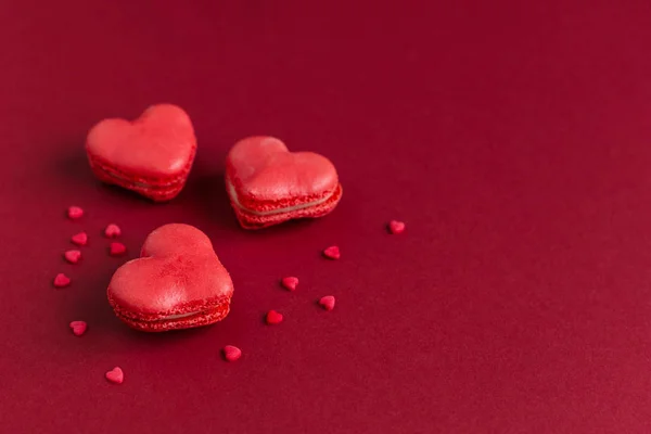Macarrones en forma de corazón sobre un fondo rojo oscuro, decorados con corazones dulces . — Foto de Stock