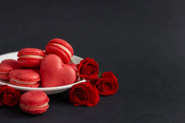 Sabrosos macarrones franceses con rosas rojas sobre un fondo negro. Concepto para el día de San Valentín . — Foto de Stock