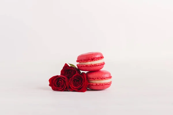 Lekkere franse macarons met rode roos op een witte houten achtergrond, versierd met zoete harten. — Stockfoto