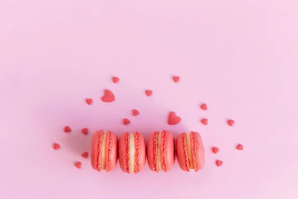 Sabrosos macarrones franceses sobre un fondo rosado, decorados con corazones dulces. Concepto para el día de San Valentín . — Foto de Stock