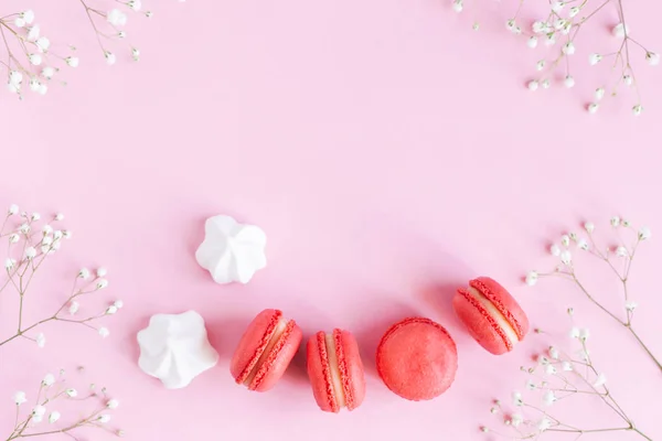 Roze macarons, witte marshmallows en bloemen op een roze pastelachtergrond. — Stockfoto