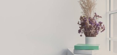 Beyaz kavanozda kurumuş çiçekler, pencereye yakın masada kitaplarla fotokopi alanı. Oturma odası, konut ya da daire için asgari ve sade dekorasyon. İleti, alıntı veya metin için boş alan