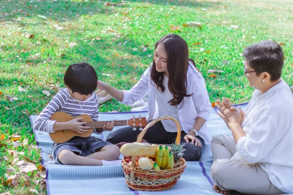 Família asiática feliz tem lazer no parque no fim de semana ou férias. A mãe ensina o filho a tocar guitarra. Avó desfrutar deste belo momento de amor. Relacionamento de geração familiar ou foto de vínculo — Fotografia de Stock