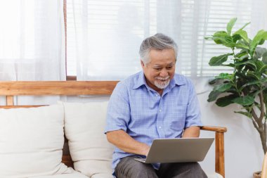 Evde bilgisayarla çalışan sağlıklı Asyalı kıdemli yaşlı bir adam. Emekli büyükbaba internetten öğrenmeyi ya da öğrenmeyi bilgisayarla öğrenmeyi seviyor. Yaşlı aktivitesi ve yaşam tarzı