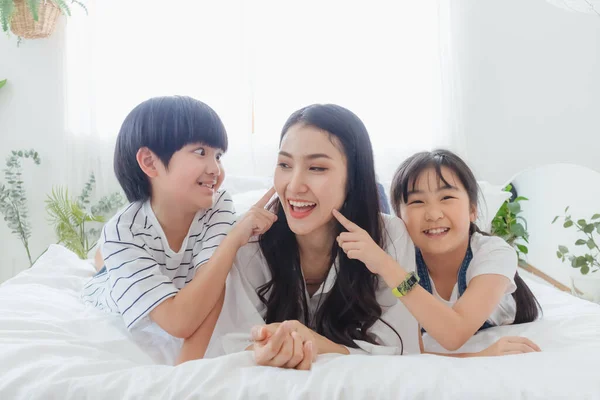 Güzel, mutlu, Asyalı bir aile sıcak bir evde. Gülümseyen anne, oğul ve kız yatak odasında eğleniyor, rahatlıyor ve oyun oynuyorlar. Mutluluk ilişkisi ve ebeveynler ve çocuklar arasındaki sevgi bağı anı