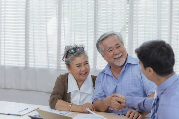 Mutlu Asyalı kıdemli yaşlı çiftler iş anlaşması ve kişisel mali danışman veya emlakçıyla el sıkışıyor. Profesyonel danışmanlık ile emeklilik yatırımı planlaması.
