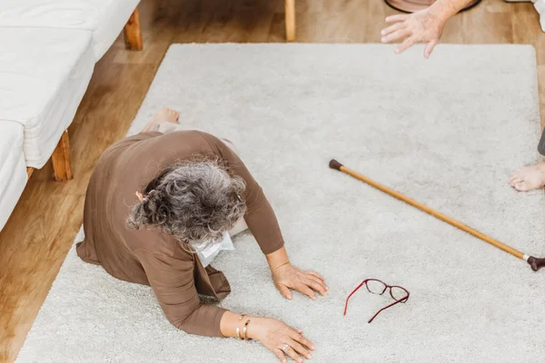 Asian senior woman falling down lying on floor at home and senior man hands try to help. Elderly woman pain and hurt from osteoporosis sickness or heart attack. Old adult life insurance concept