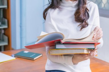 Genç Asyalı kız öğrenci portresi oturur ve üniversite kütüphanesinde sınavlara ya da sınavlara hazırlanmak için ders kitabı okumaya konsantre olur. Eğitim bilgisi ve öğrenme kavramı.